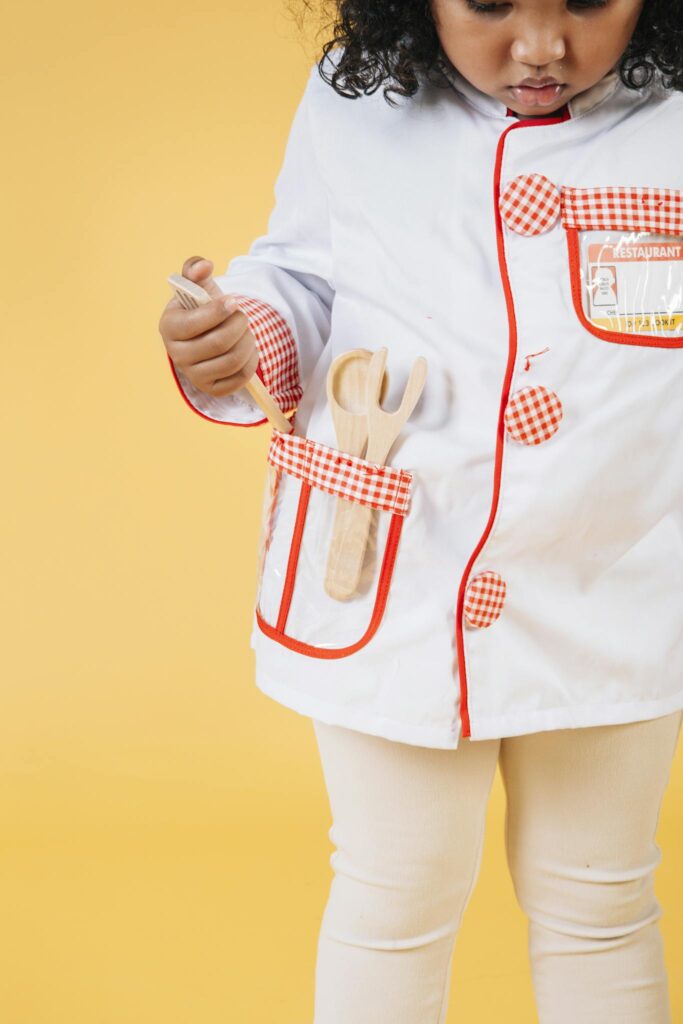 Cute black girl in uniform with kitchen accessories