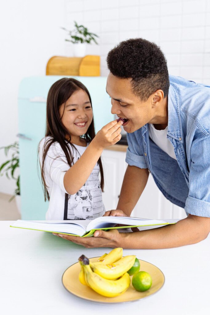 A father and daughter enjoy cooking together in a bright, modern kitchen setting.